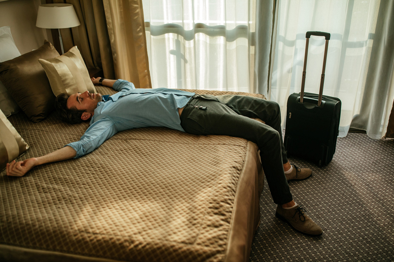 man laying on hotel bed with suitcase next to him